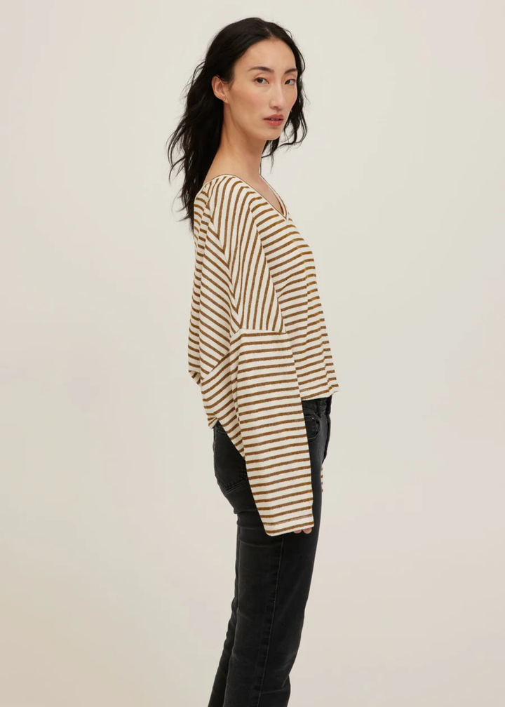 A woman modeling a beige and brown horizontally striped long-sleeve top with black jeans, shown from a side profile against a plain light background.
