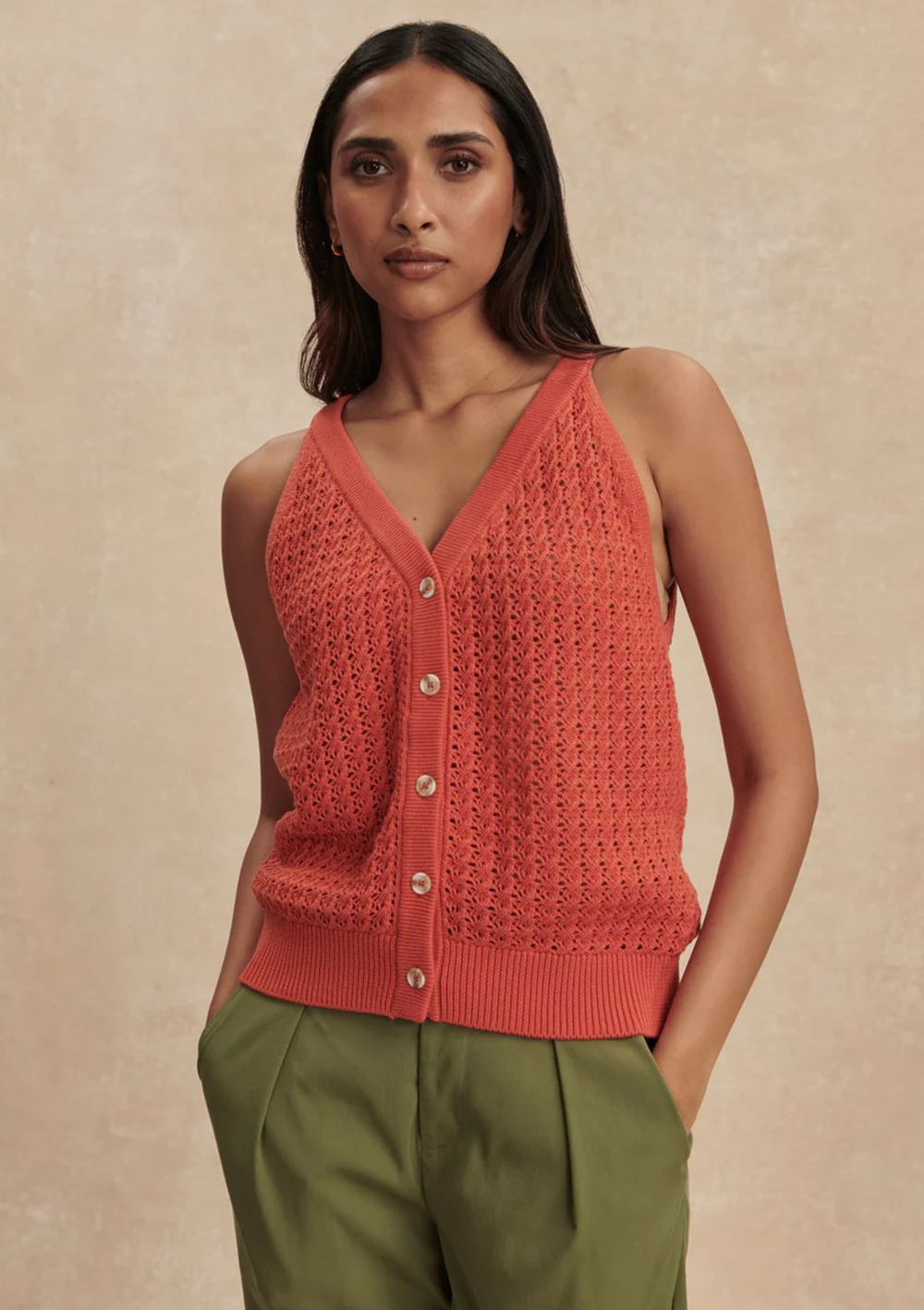 Woman wearing a coral knitted vest against a beige background