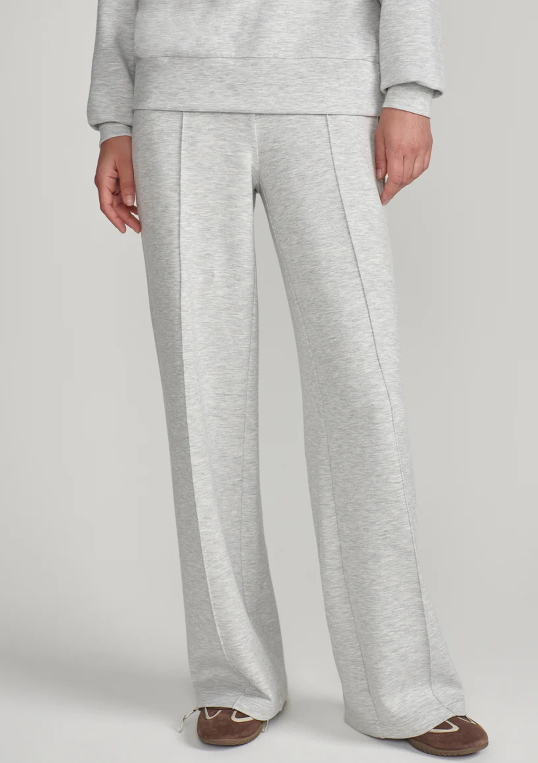 A person wearing light heather gray wide-leg sweatpants with a matching sweatshirt partially visible, standing against a plain light gray studio background.