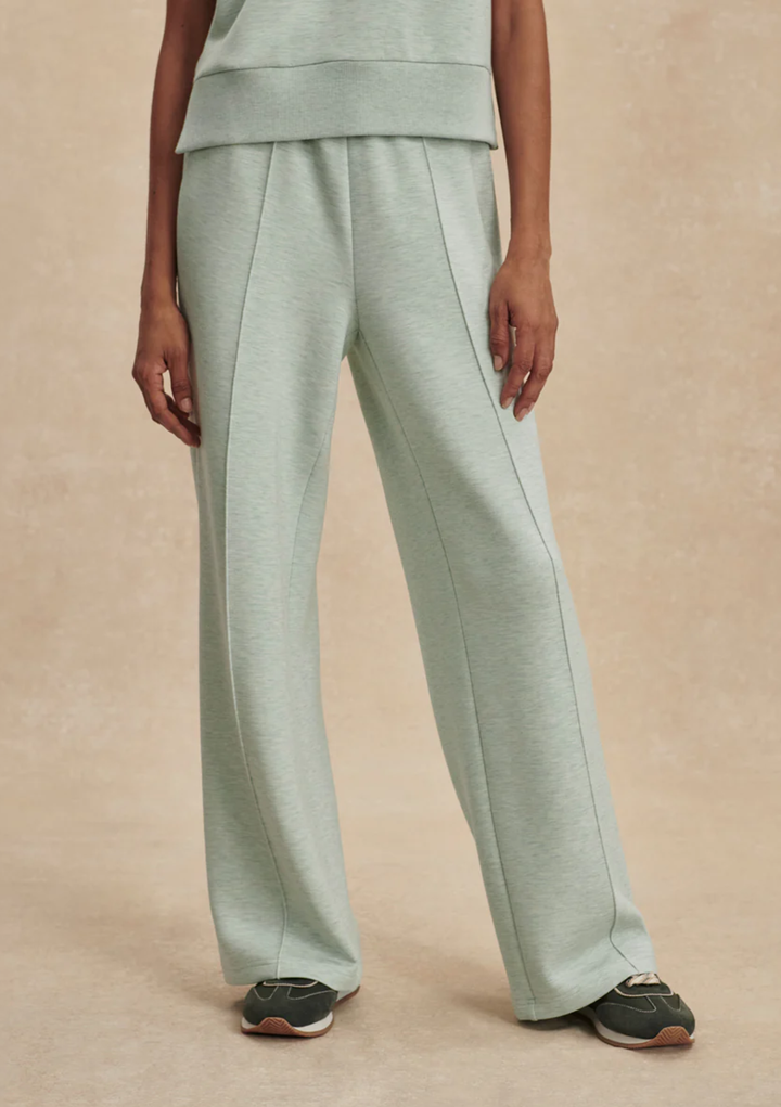 A person wearing light sage green wide-leg sweatpants with a matching cropped top, shown from the waist down against a warm beige studio background.