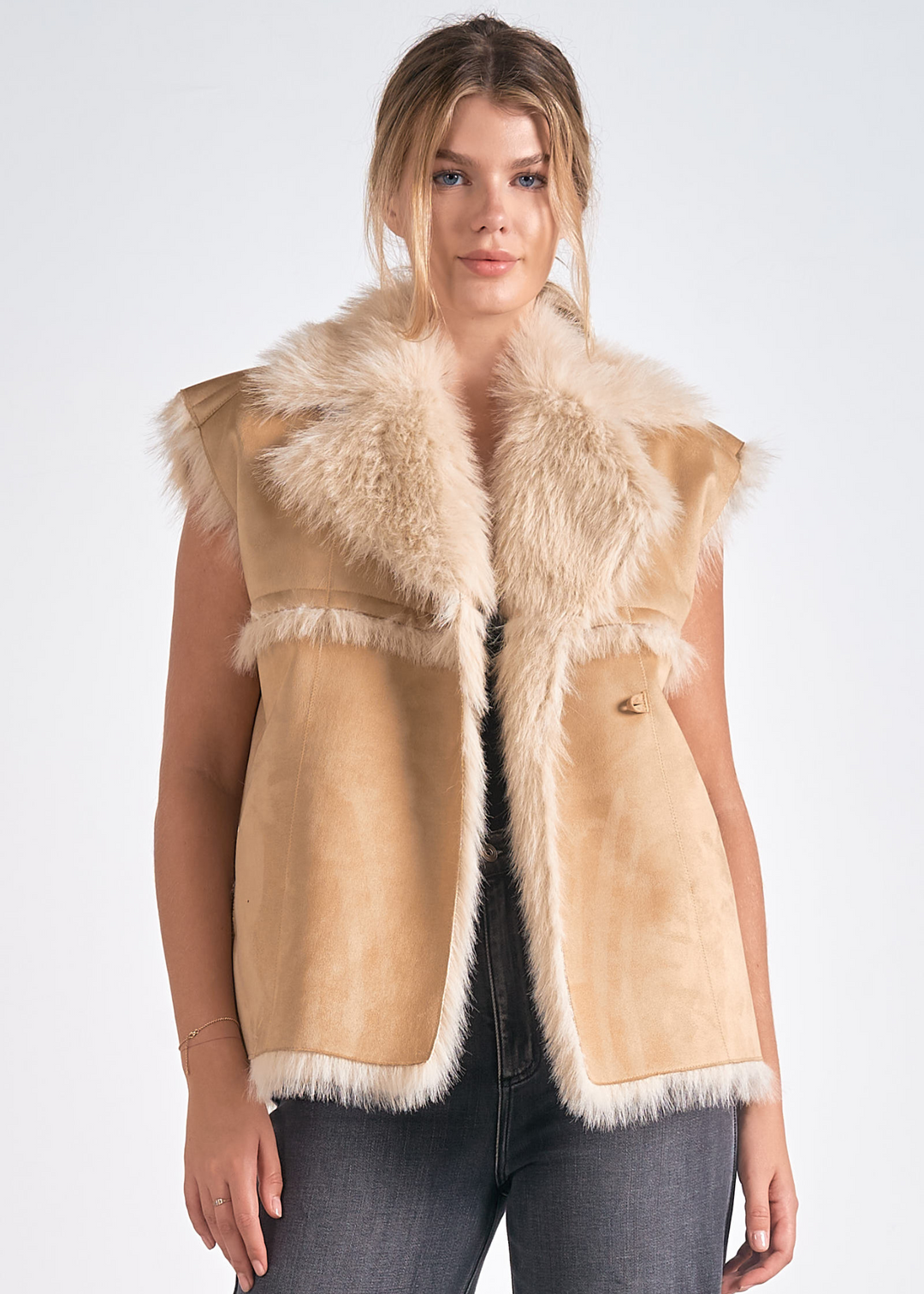 Woman wearing a stylish tan faux fur-trimmed sleeveless vest with a fluffy collar, paired with dark jeans, showcasing a cozy and chic winter look