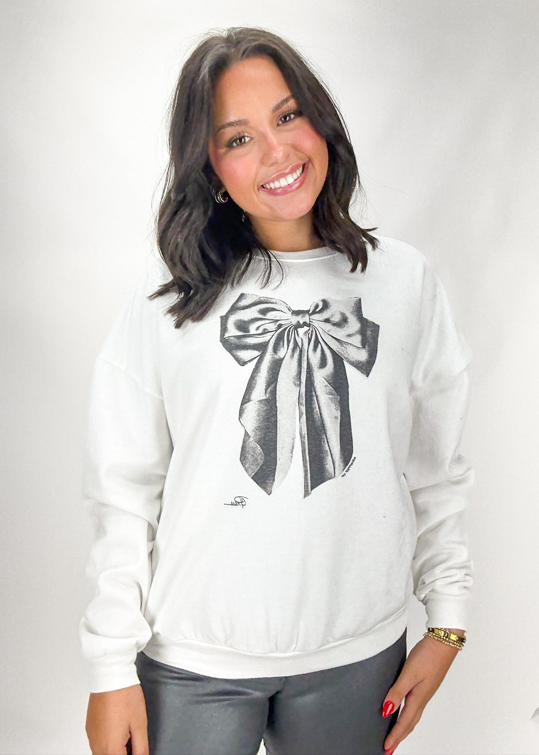 Woman wearing a white sweatshirt with a black bow design on a plain background