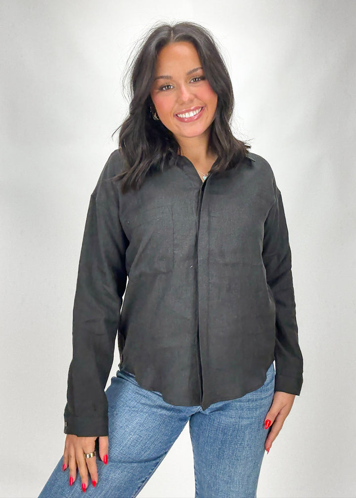 Woman wearing a dark gray button-up shirt and blue jeans on a white background