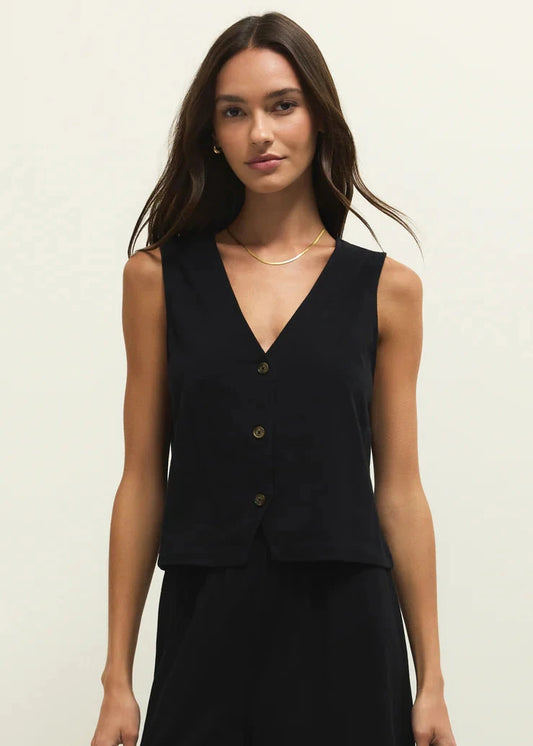 Woman wearing a black sleeveless top with buttons on a plain background