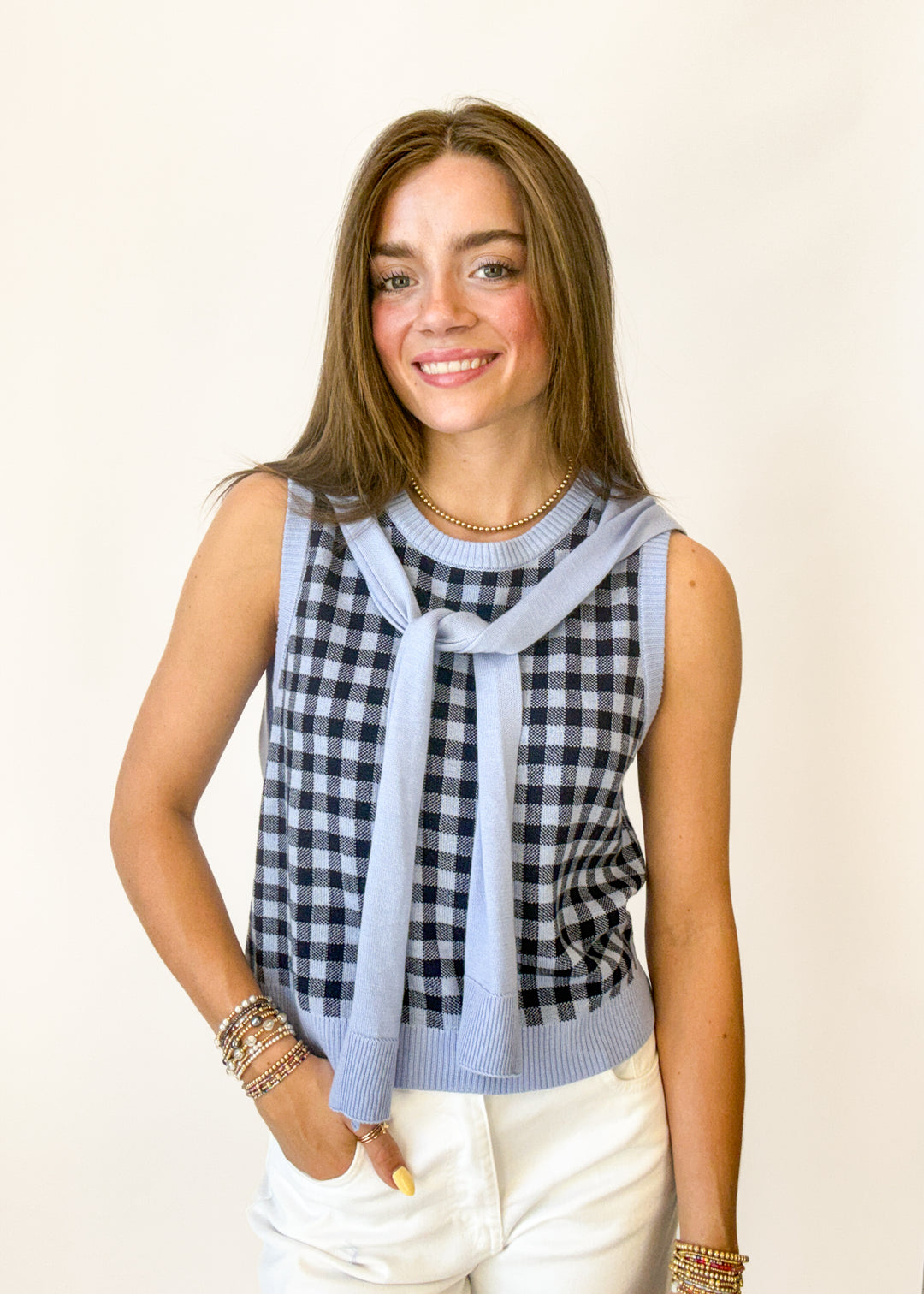 Woman wearing a checkered top with a light blue scarf against a plain background