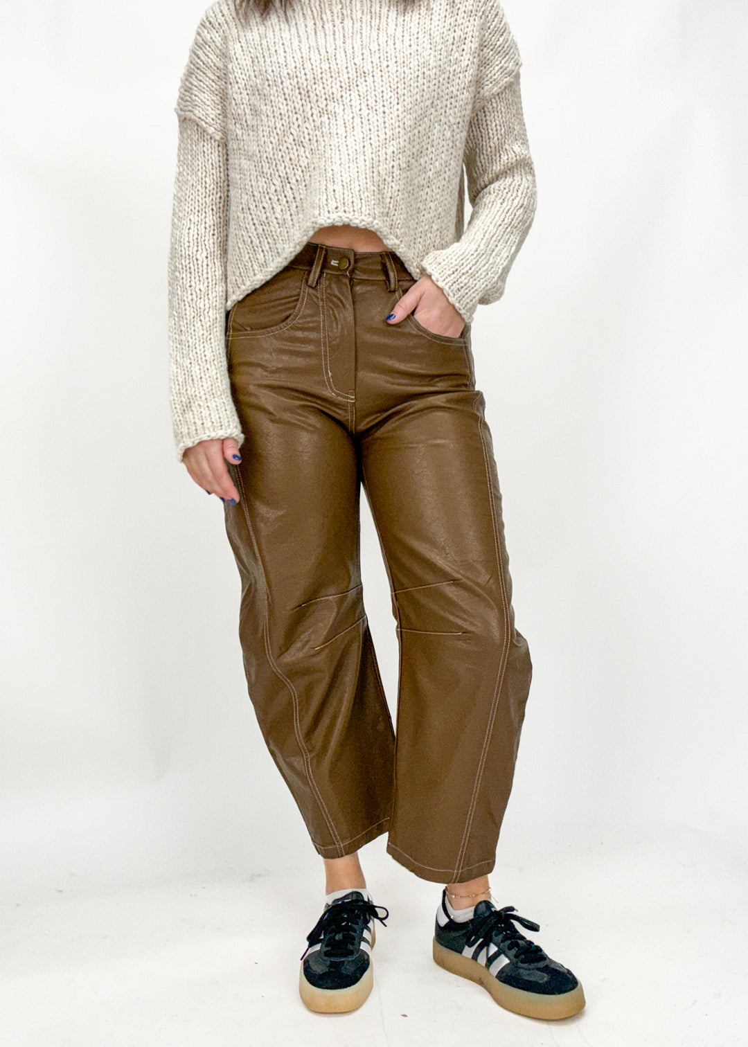 Person wearing brown leather pants and a beige sweater on a white background