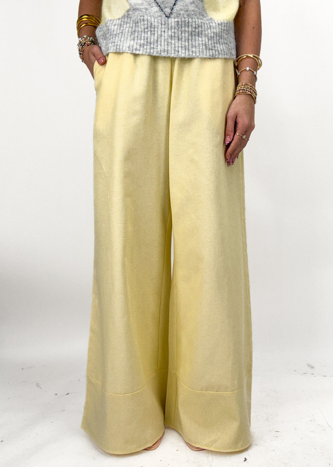 Person wearing a light yellow outfit with wide-leg pants on a white background