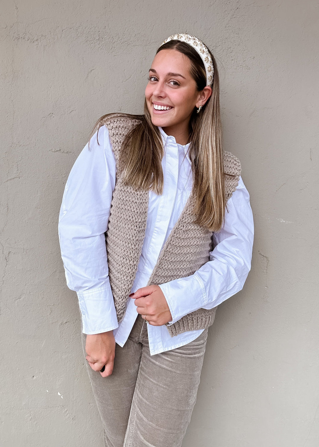 Knit cardigan vest in a taupe textured knit, layered over a white collared button-down shirt and paired with corduroy pants