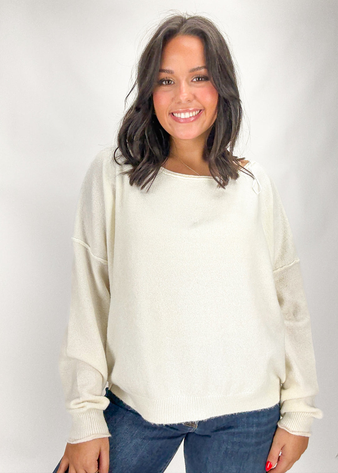 Woman wearing a cream sweater and blue jeans against a white background