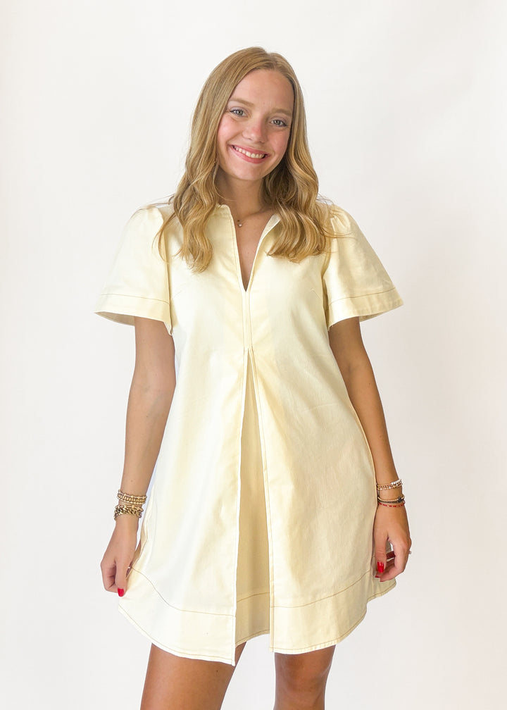 Woman wearing a cream dress with front pleats on a white background
