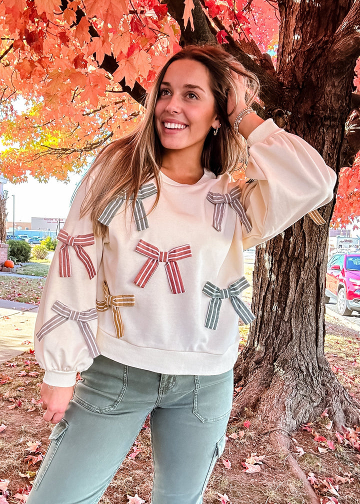 Women's cream sweatshirt with multi-colored bow accents styled with sage green cargo pants