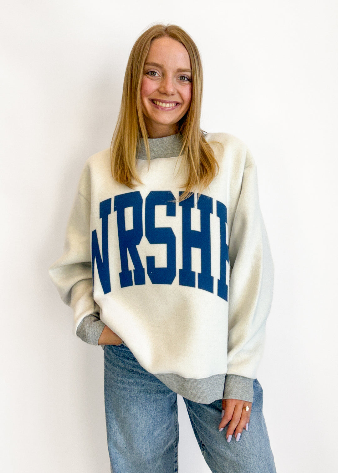 Person wearing a white sweater with 'NURSHE' printed on it against a plain background