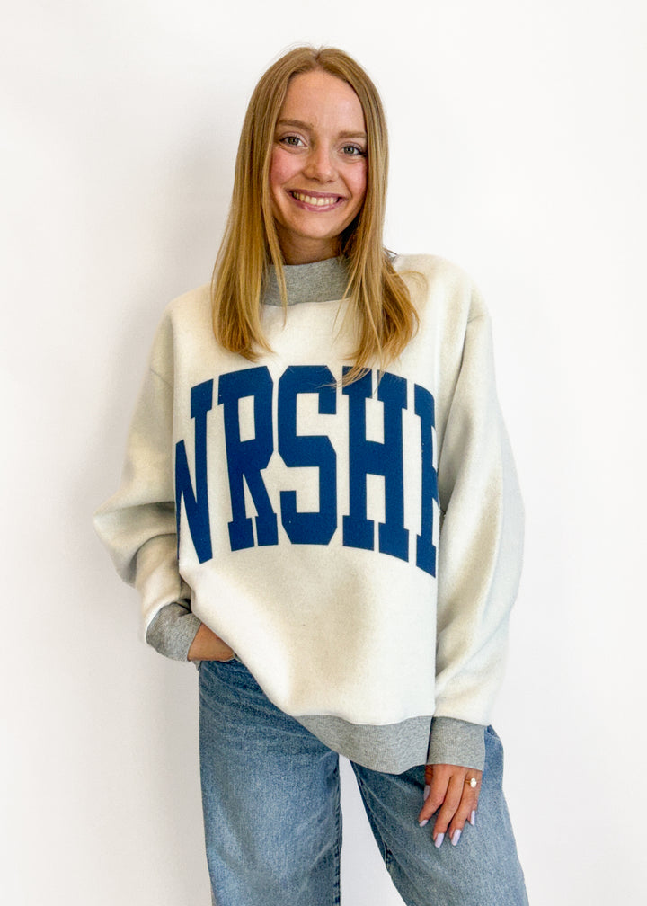 Person wearing a white sweater with 'NURSHE' printed on it against a plain background