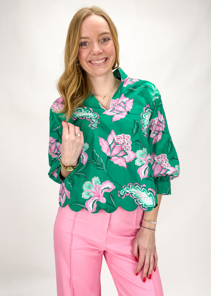 Woman wearing a green floral blouse and pink pants against a white background