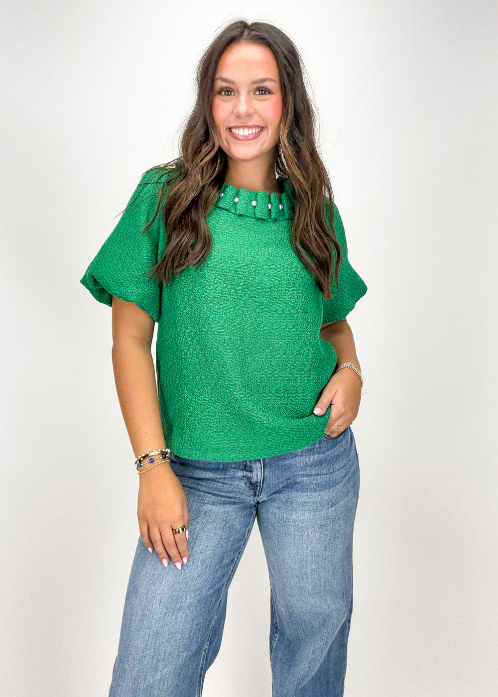 Woman wearing a green top with studded details and blue jeans 