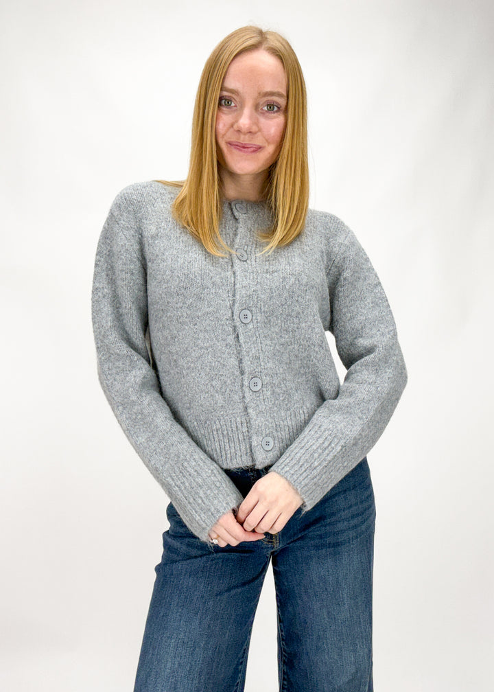 Person wearing a gray cardigan and blue jeans on a white background