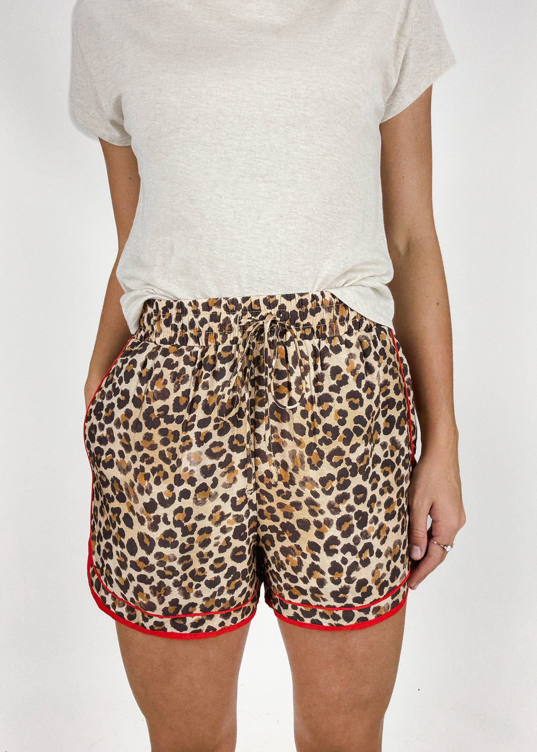 woman wearing leopard print drawstring shorts with red trim styled with heather white tee