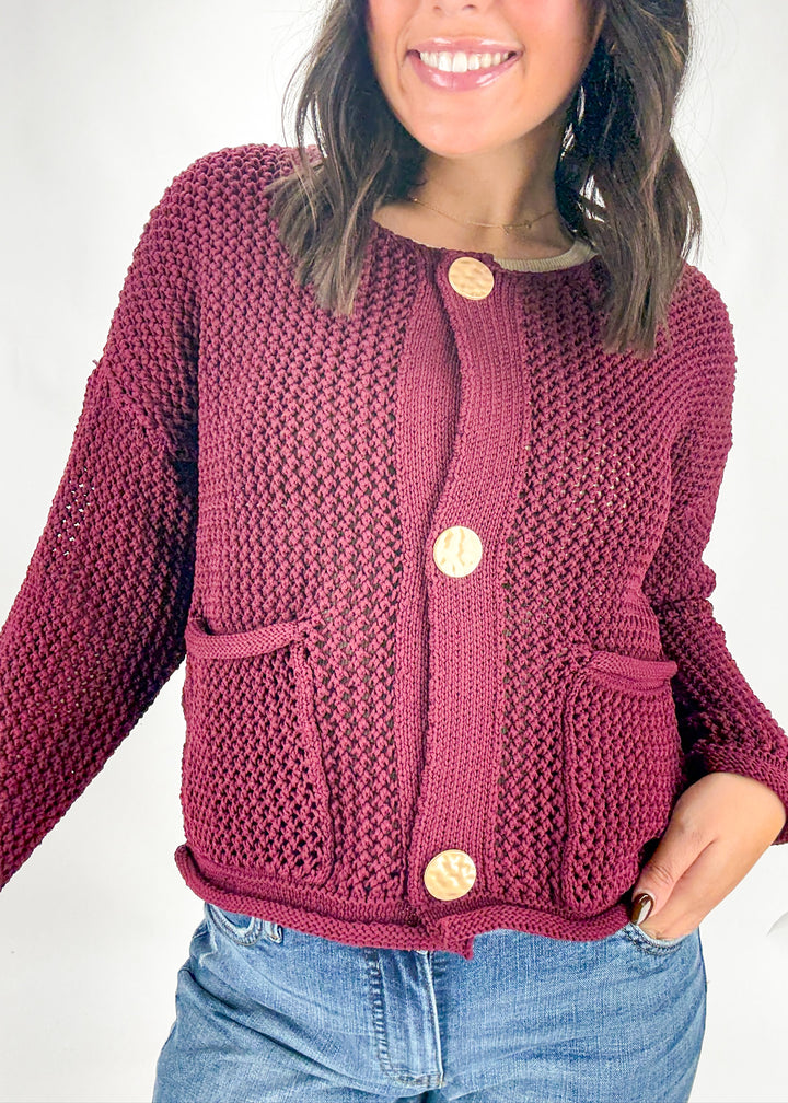 Person wearing a maroon knitted cardigan with gold buttons on a white background