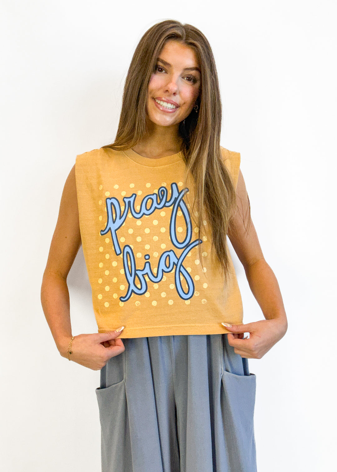 Woman wearing a mustard yellow sleeveless top with 'Pray Big' text on a white background