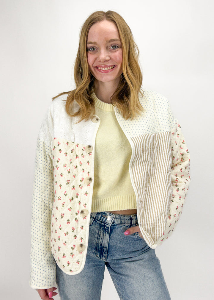 Woman wearing a cream cardigan with floral patterns, yellow sweater, and blue jeans on a white background