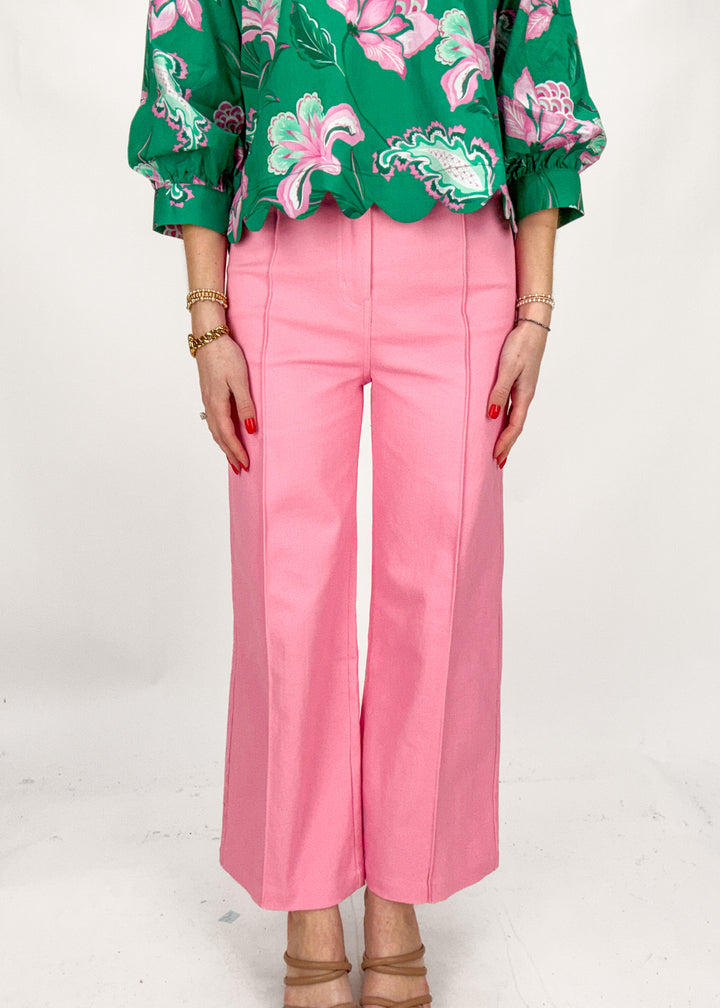 Person wearing a green floral blouse and pink pants on a white background