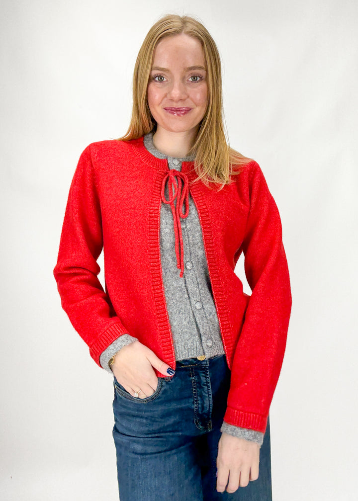 Woman wearing a red cardigan over a gray sweater with a white background