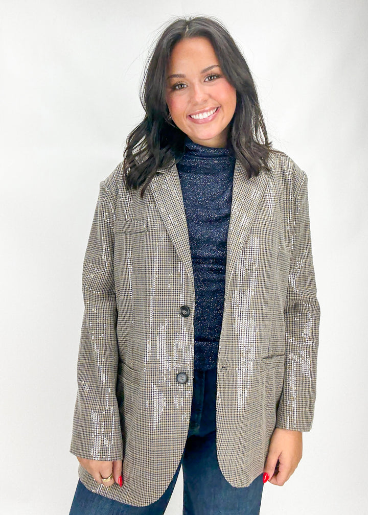 Woman wearing a checkered blazer over a blue sweater and jeans on a white background