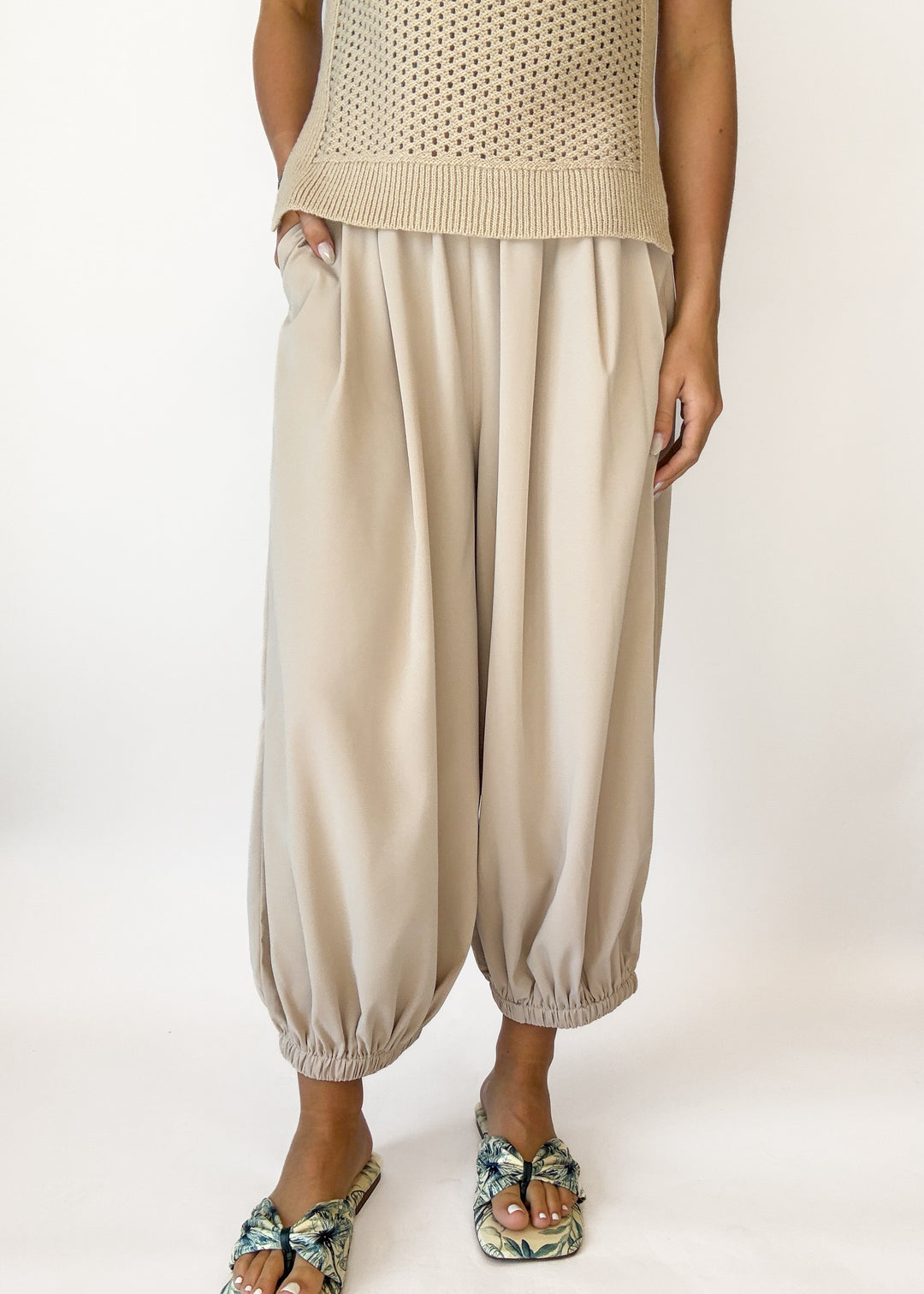 Person wearing a beige knitted top and wide-leg pants on a white background