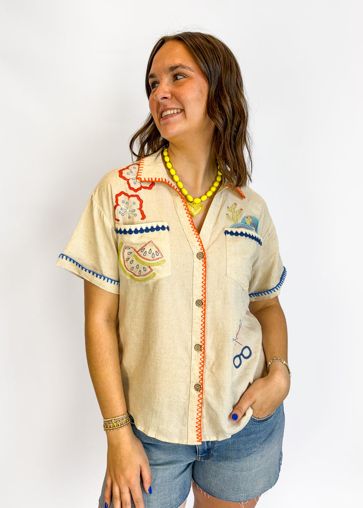 Woman wearing a decorative beige shirt with colorful patterns on a white background
