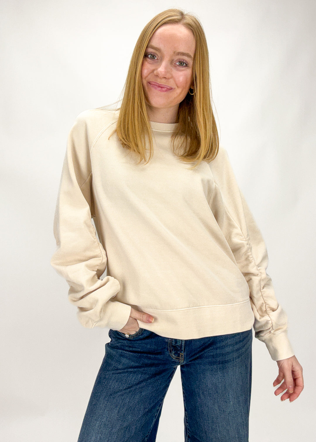 Woman wearing a beige sweater and blue jeans on a white background