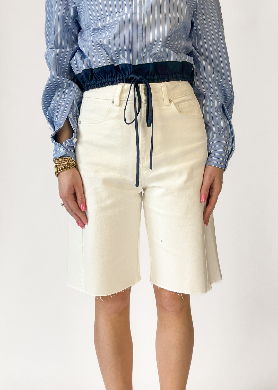 Person wearing a blue striped shirt and white shorts on a white background