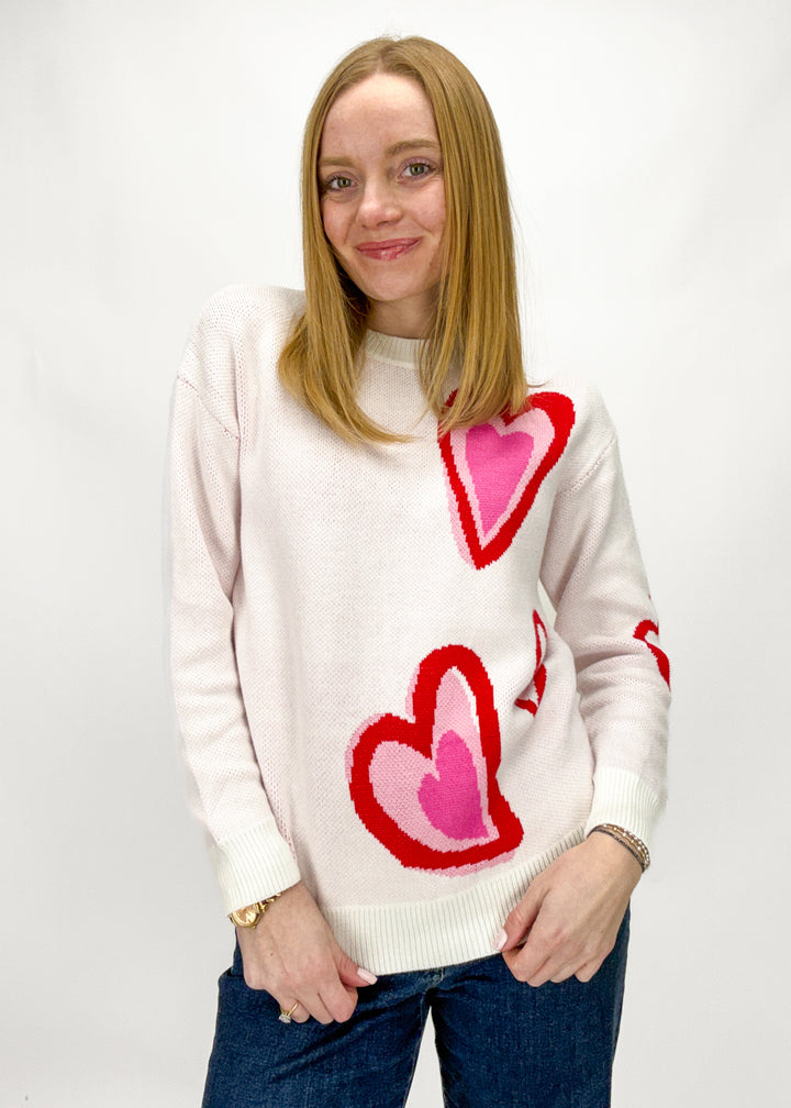 Person wearing a white sweater with red and pink heart patterns on a plain background