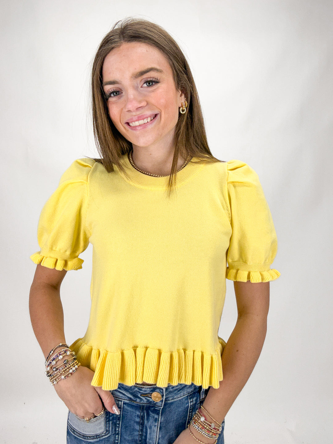Woman wearing a yellow blouse with ruffled sleeves on a plain background