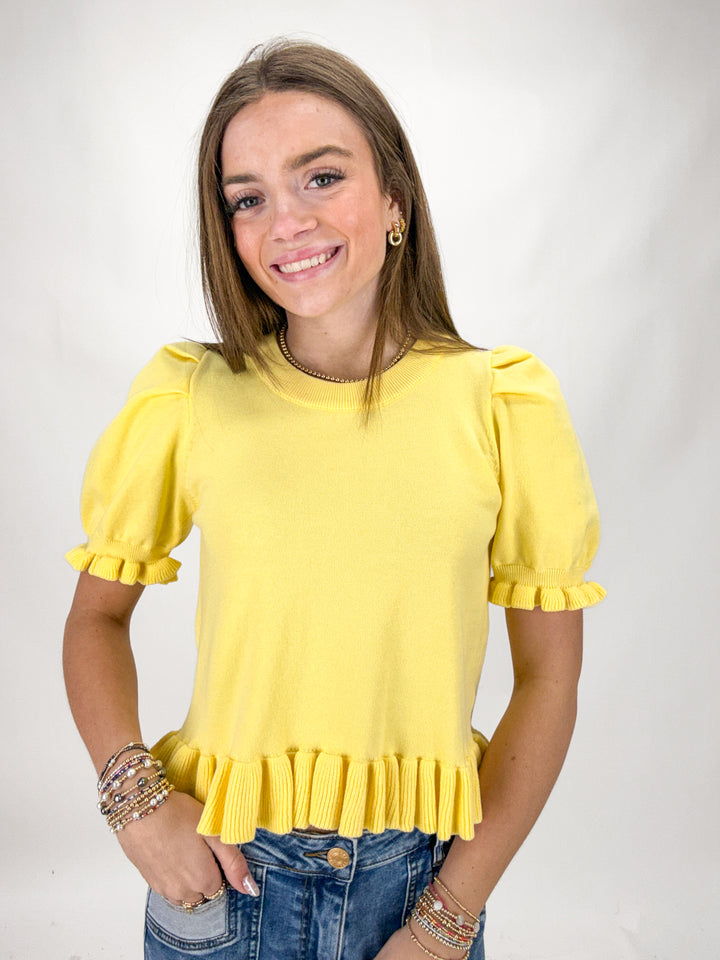 Woman wearing a yellow blouse with ruffled sleeves on a plain background